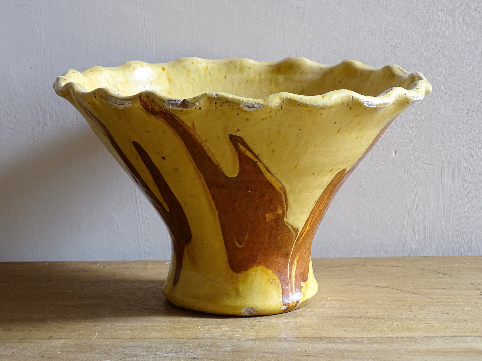 French antique terracotta bowl with yellow glaze, this earthenware basin has sweeps of a red-brown tone to the body and a crimped, pie crust style edge.