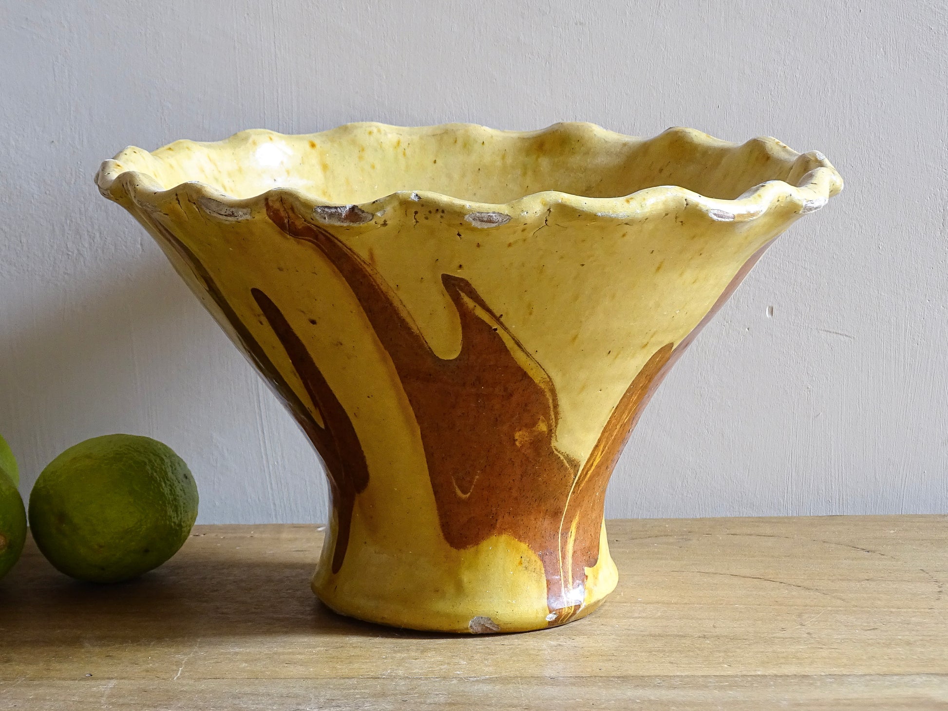 French antique terracotta bowl with yellow glaze, this earthenware basin has sweeps of a red-brown tone to the body and a crimped, pie crust style edge.