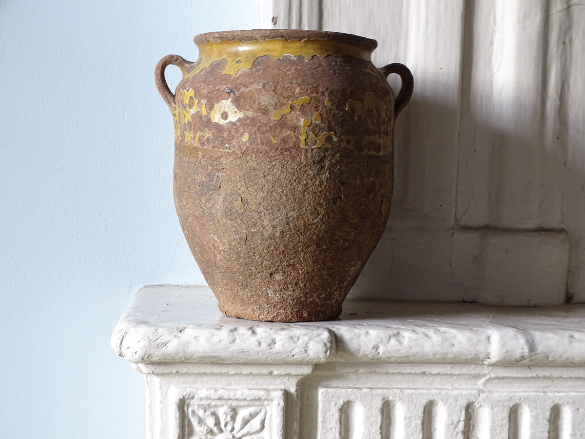 French antique confit pot with worn yellow glaze on an old country fireplace