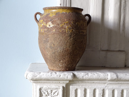 French antique confit pot with worn yellow glaze on an old country fireplace