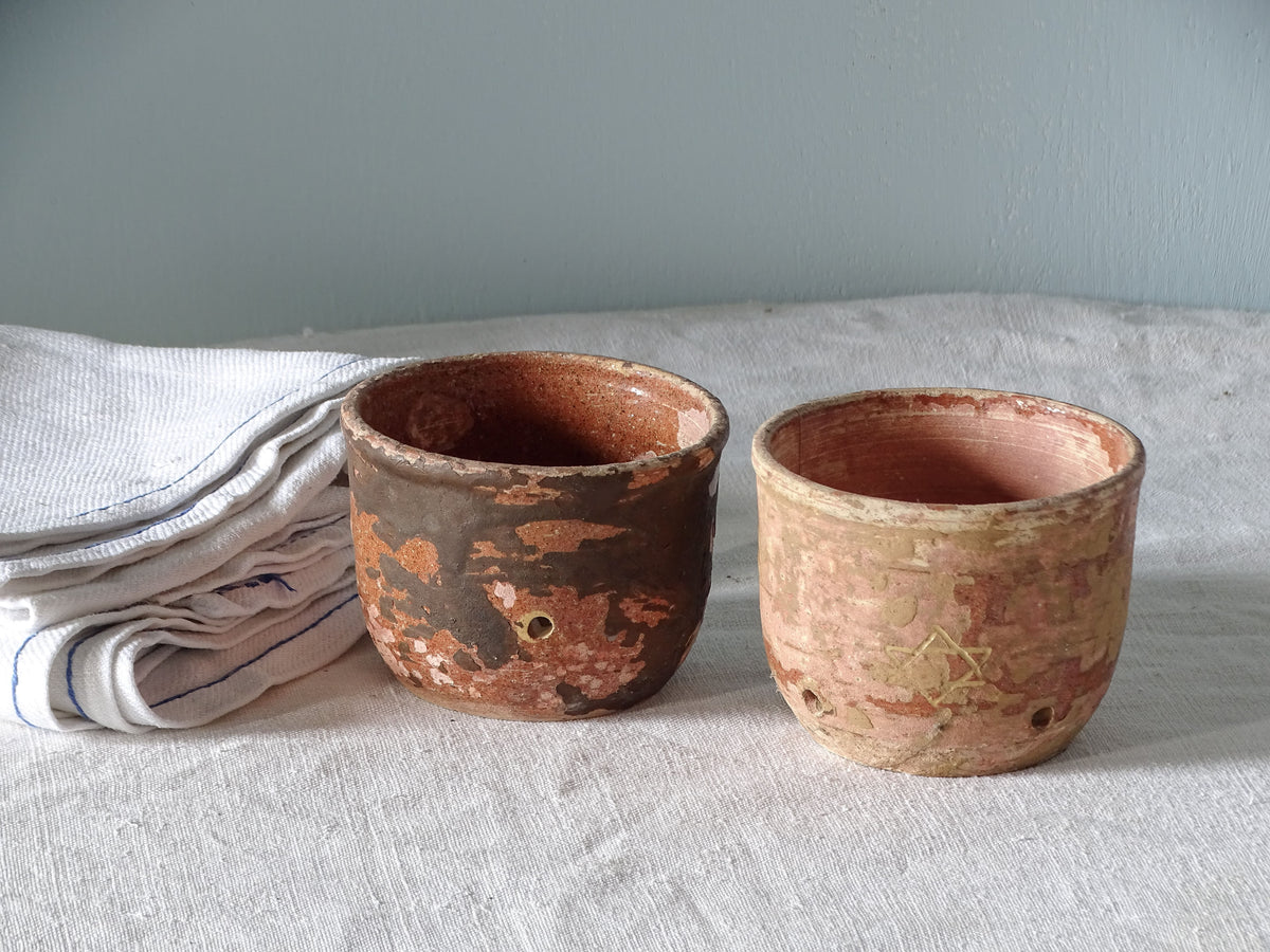 French antique earthenware faisselles, pictured on a table with antique linen in front of a pale blue wall