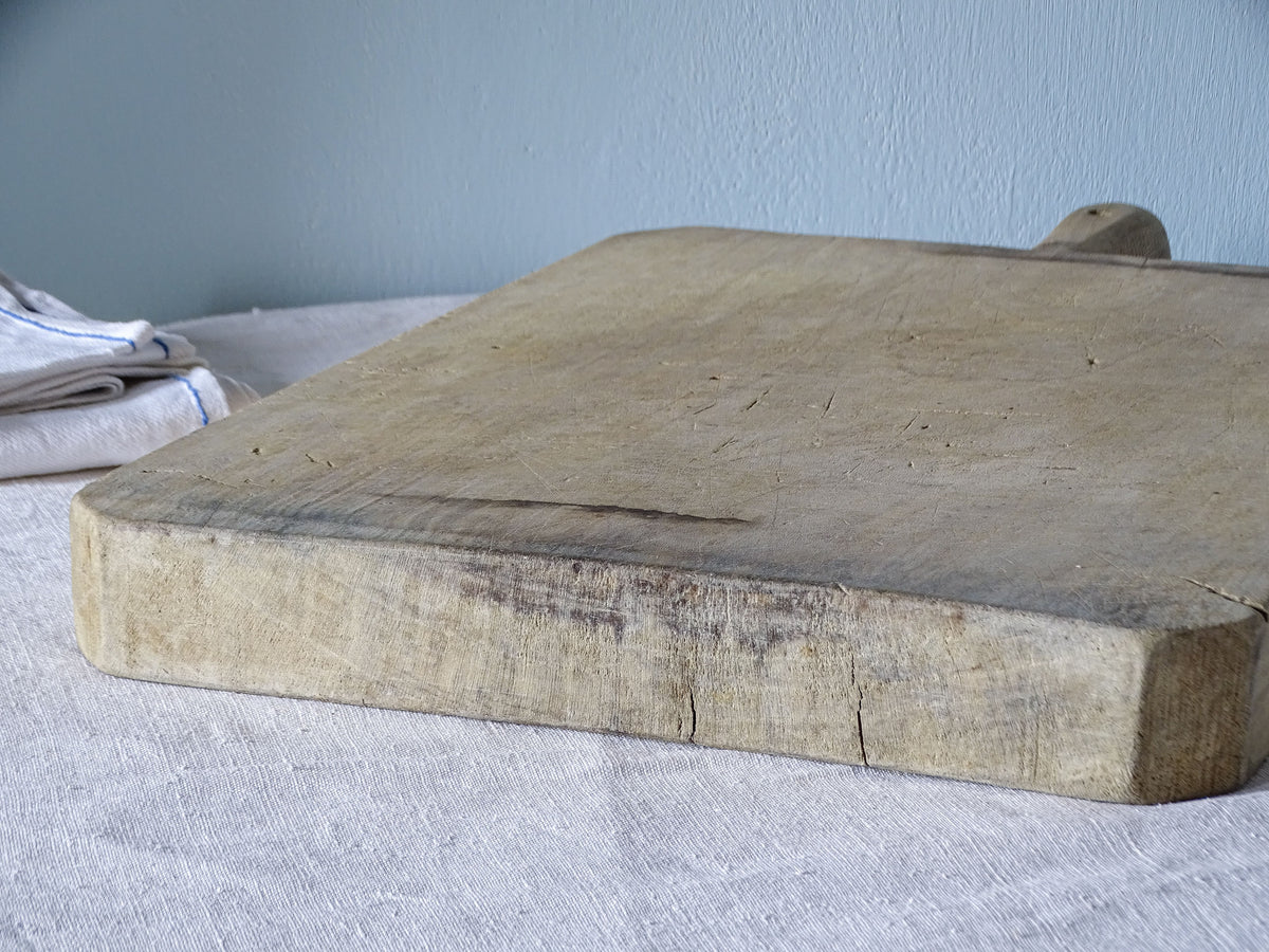 Side view of vintage French wooden chopping board showing substantial thickness, darkened patina and small cracks.