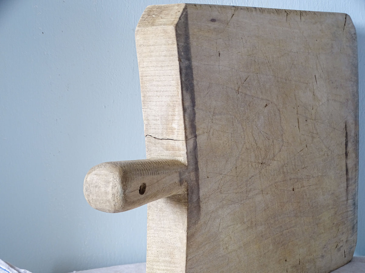 Close-up of rounded wooden handle with hanging hole and darkened edge on vintage French cutting board.