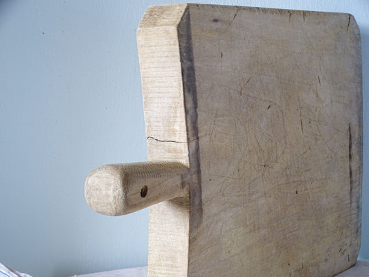 Close-up of rounded wooden handle with hanging hole and darkened edge on vintage French cutting board.