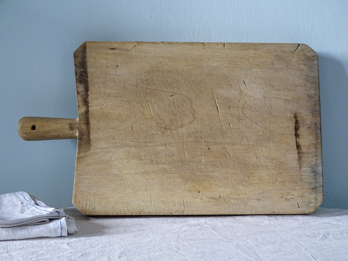 Vintage French wooden cutting board with rounded handle, rectangular shape and heavily worn knife-marked surface.