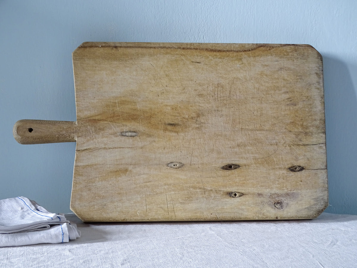 Reverse of vintage French wooden chopping board showing pale wood grain, natural knots and age-related splits.