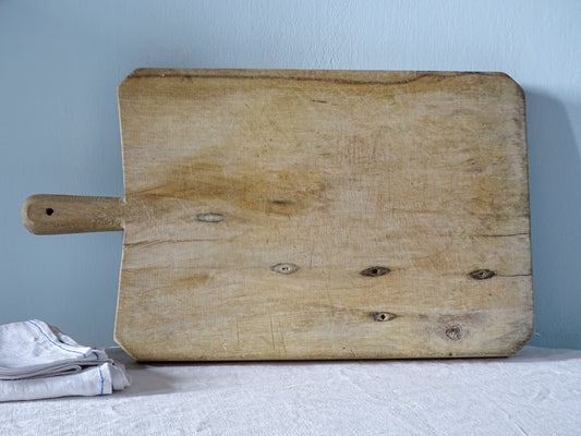 Reverse of vintage French wooden chopping board showing pale wood grain, natural knots and age-related splits.