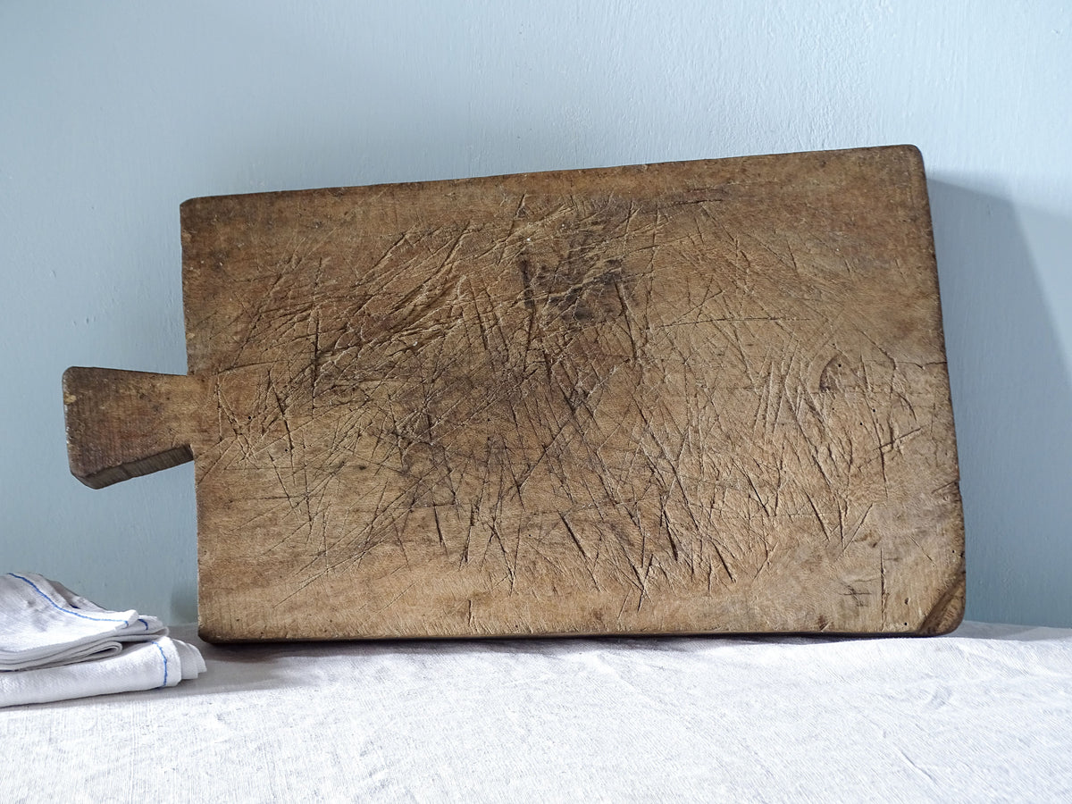 Large antique French wooden chopping board, c.1900, with short handle and heavily worn surface covered in knife marks.