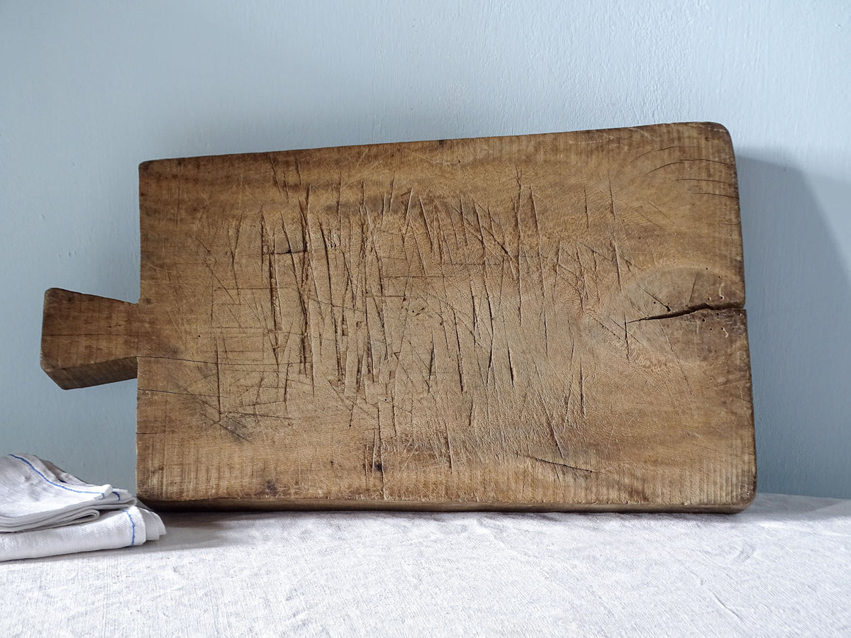 Reverse side of a rustic antique French chopping board showing decades of knife marks, aged wood and a natural split.