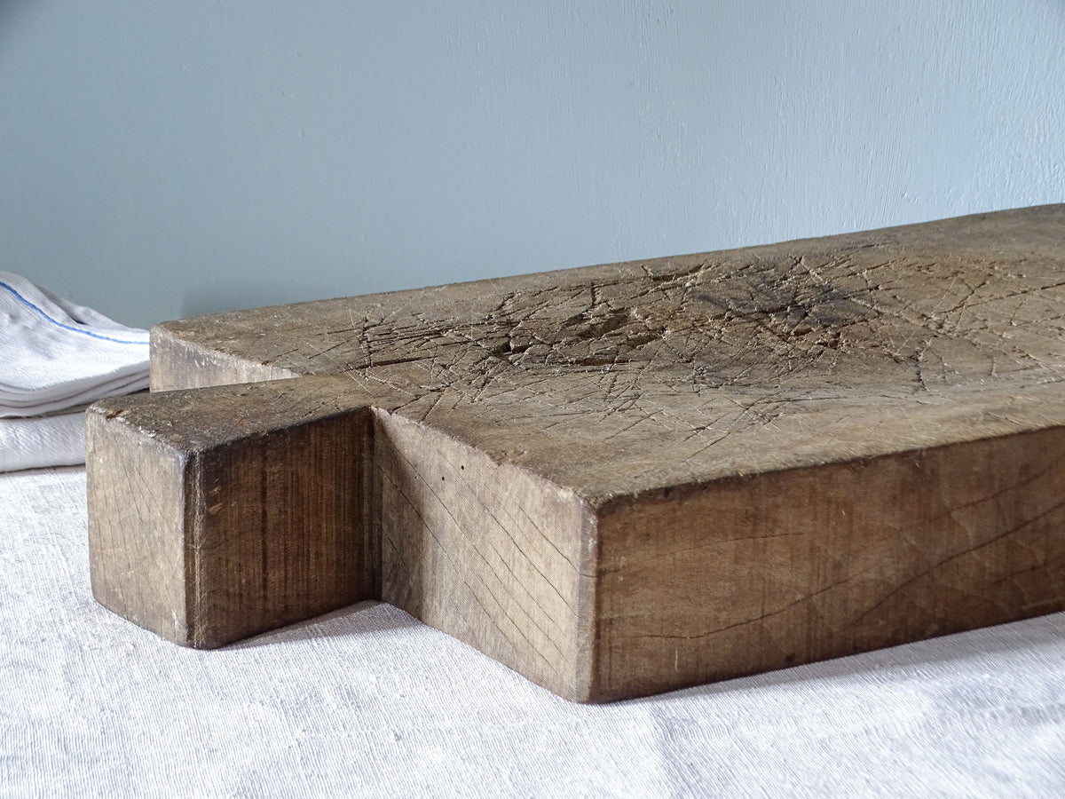 Angled view of an antique French wooden chopping block showing its substantial thickness, integral handle and worn surface.