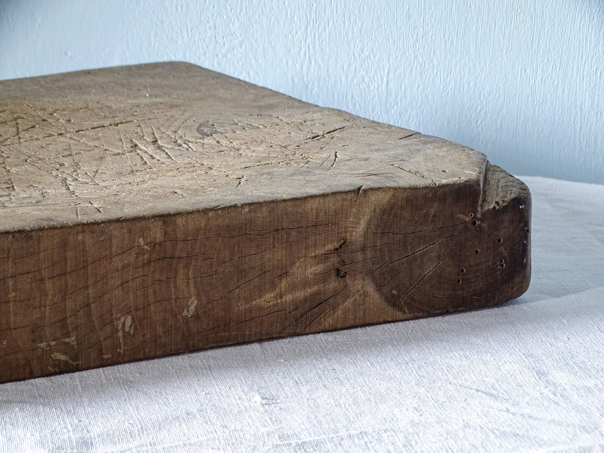 Close-up of the thick wooden edge and rounded corner of a large antique French chopping board with aged patina.
