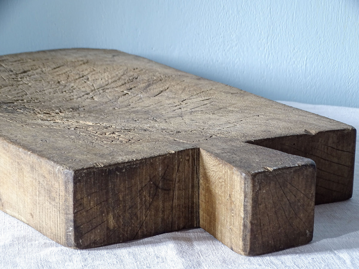 Side view of a thick antique French wooden chopping board showing the short handle, solid construction and knife-worn surface.
