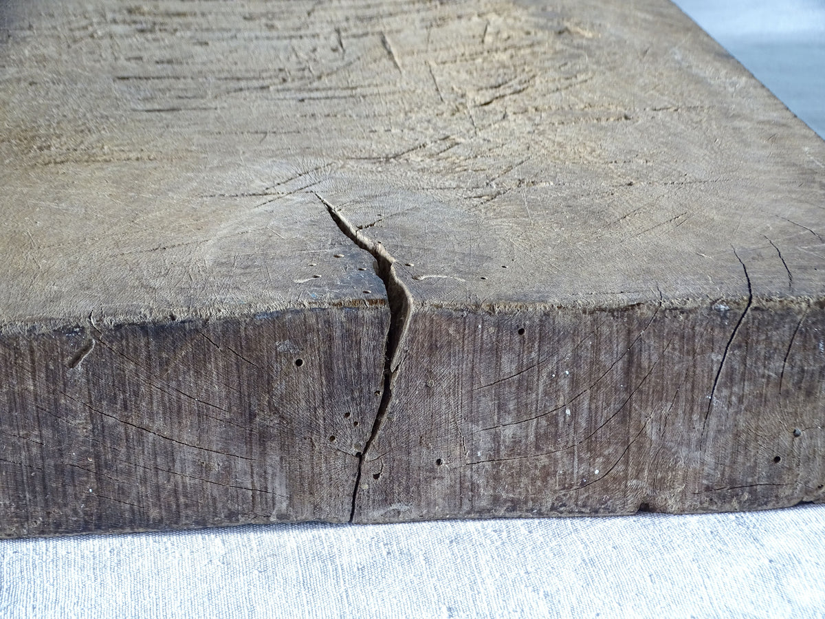 Detail of a stable age-related split, historic woodworm holes and worn wood grain on an antique French chopping block.