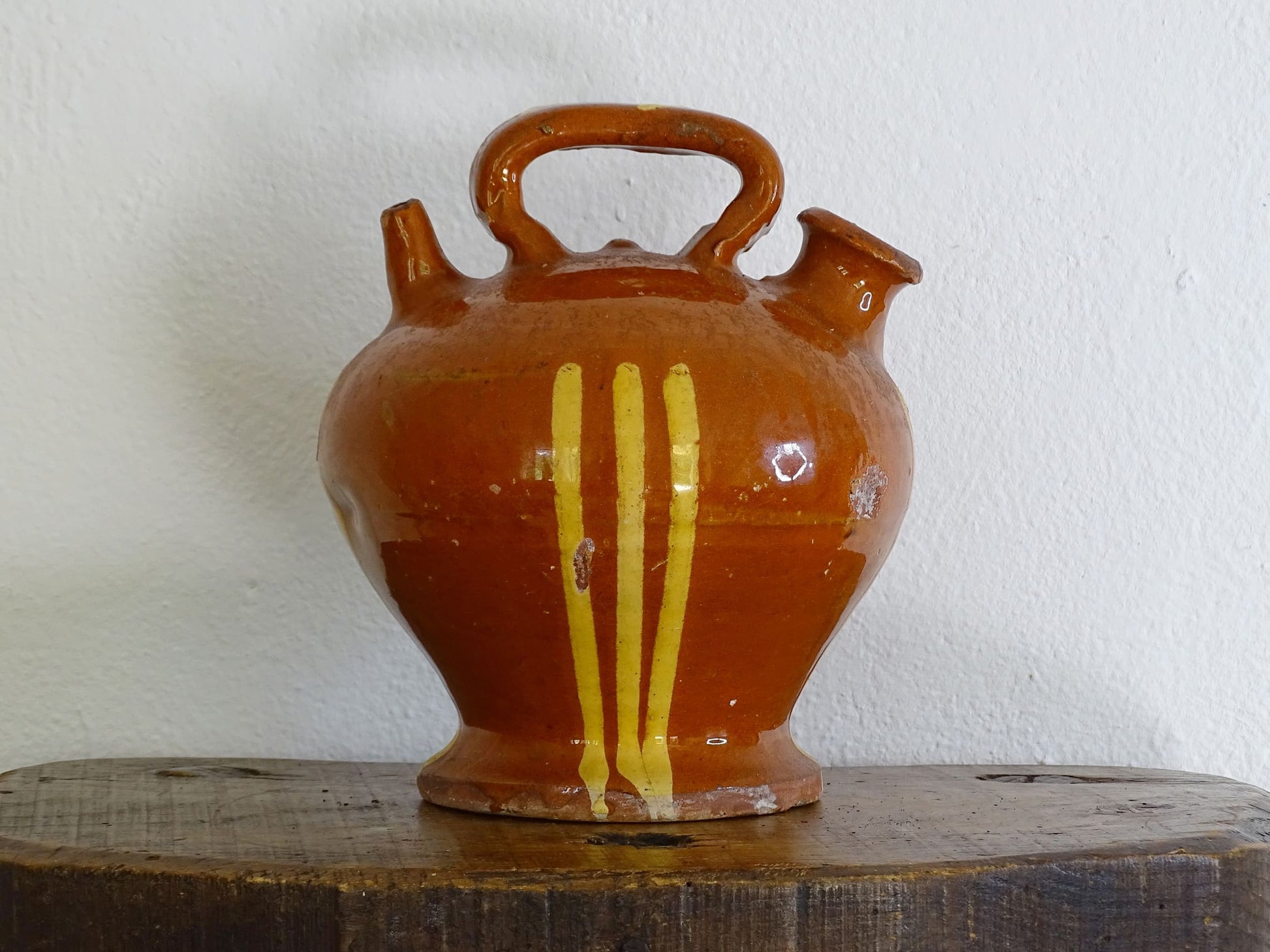 French antique pottery jug with russet glaze and yellow stripes. There is a handle to the top of this rustic terracotta earthenware pitcher and two spouts. 