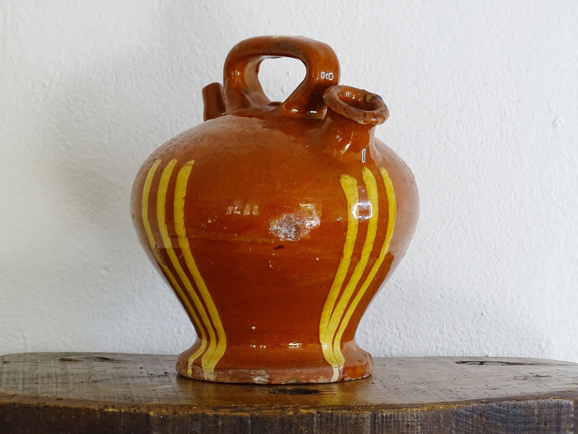 French antique pottery jug with russet glaze and yellow stripes. There is a handle to the top of this rustic terracotta earthenware pitcher and two spouts.