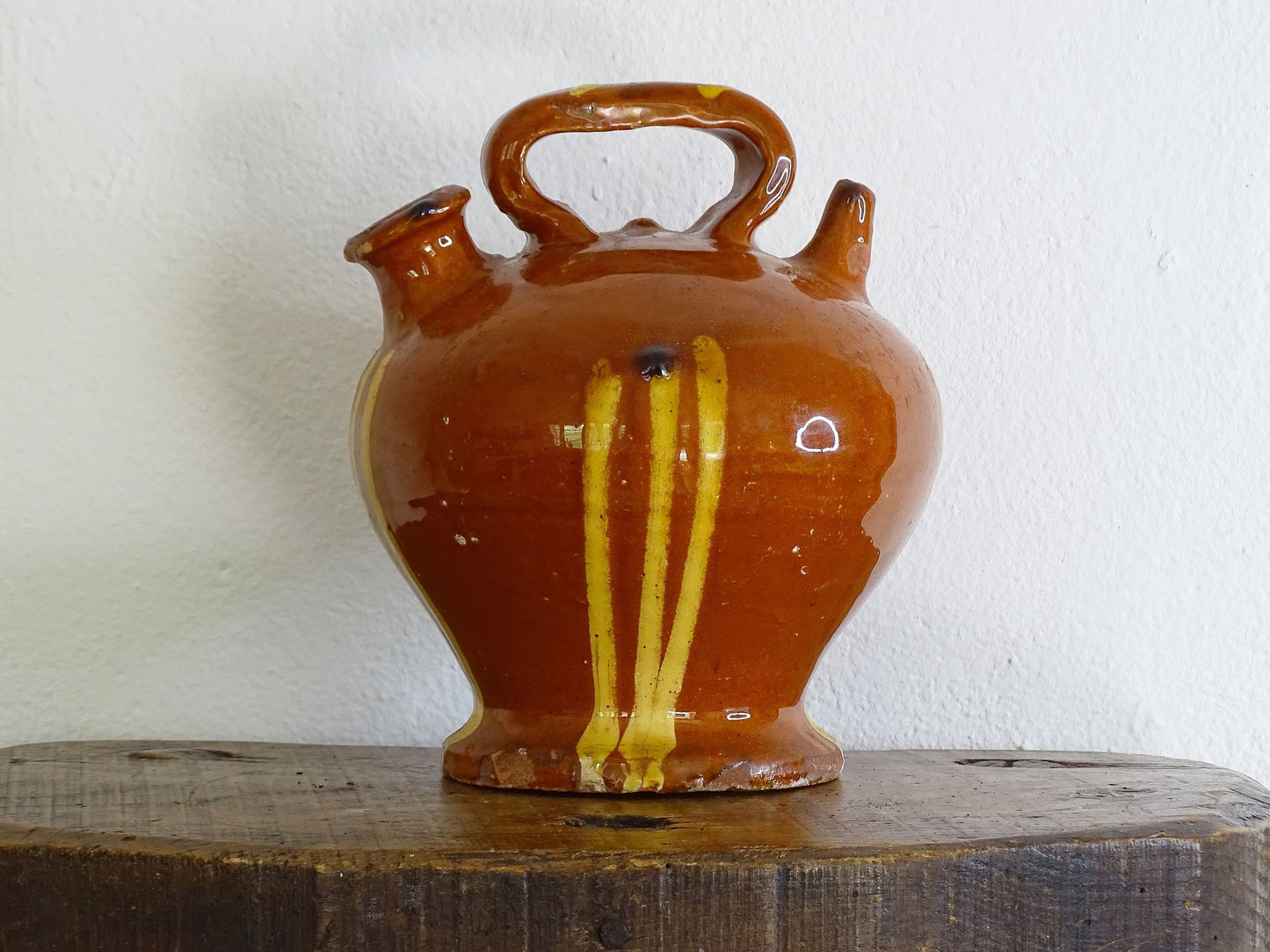 French antique pottery jug with russet glaze and yellow stripes. There is a handle to the top of this rustic terracotta earthenware pitcher and two spouts.