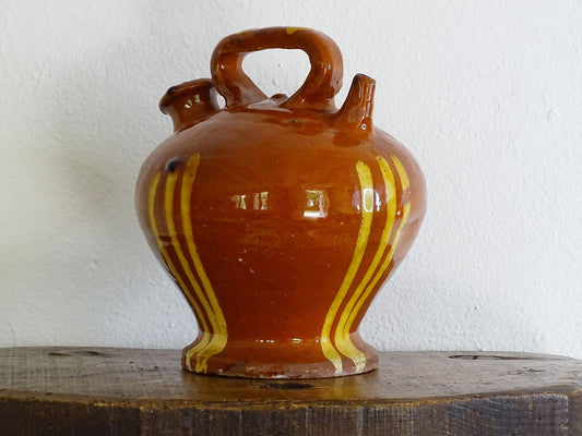 French antique pottery jug with russet glaze and yellow stripes. There is a handle to the top of this rustic terracotta earthenware pitcher and two spouts.