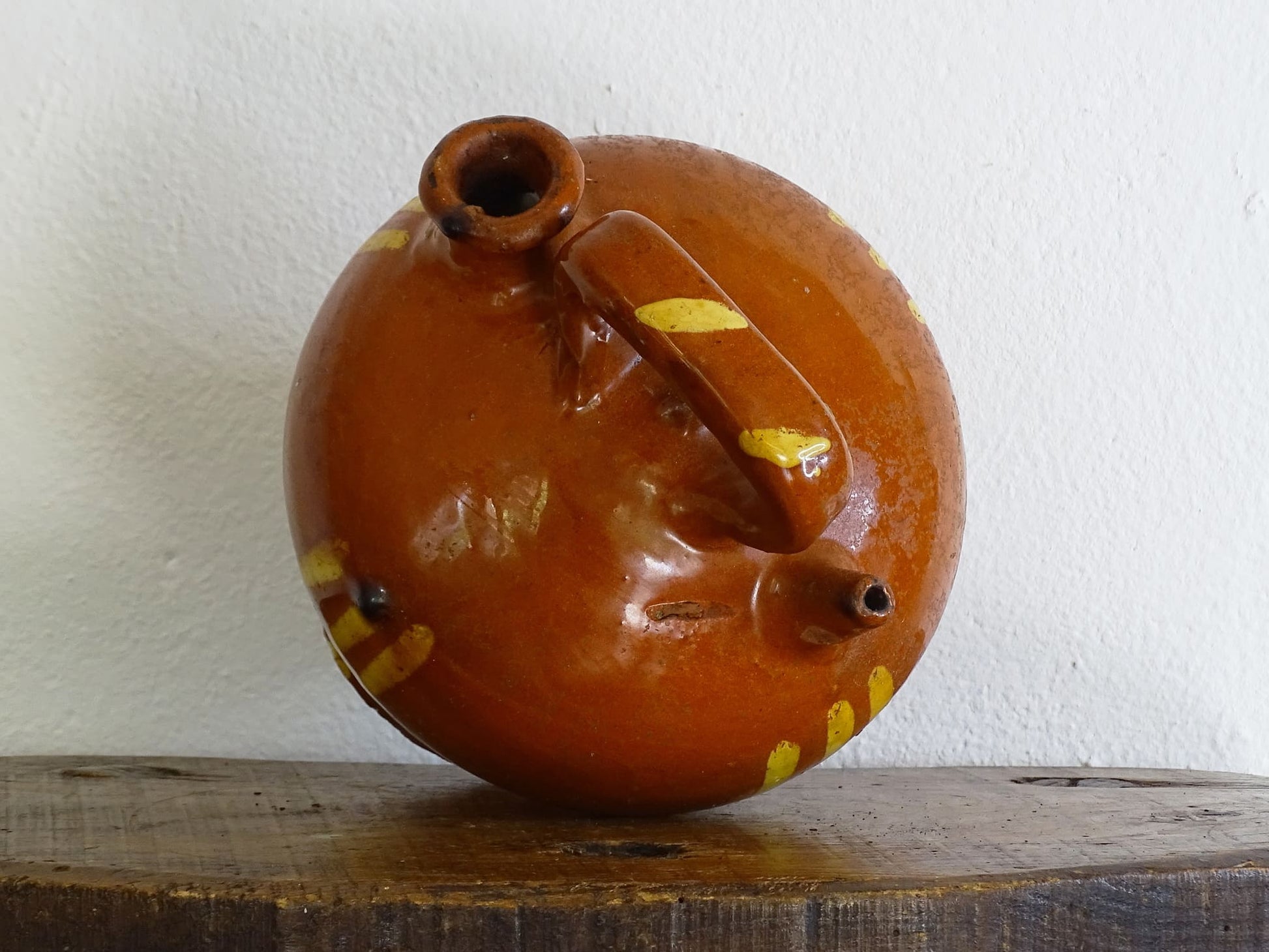 French antique pottery jug with russet glaze and yellow stripes. There is a handle to the top of this rustic terracotta earthenware pitcher and two spouts.