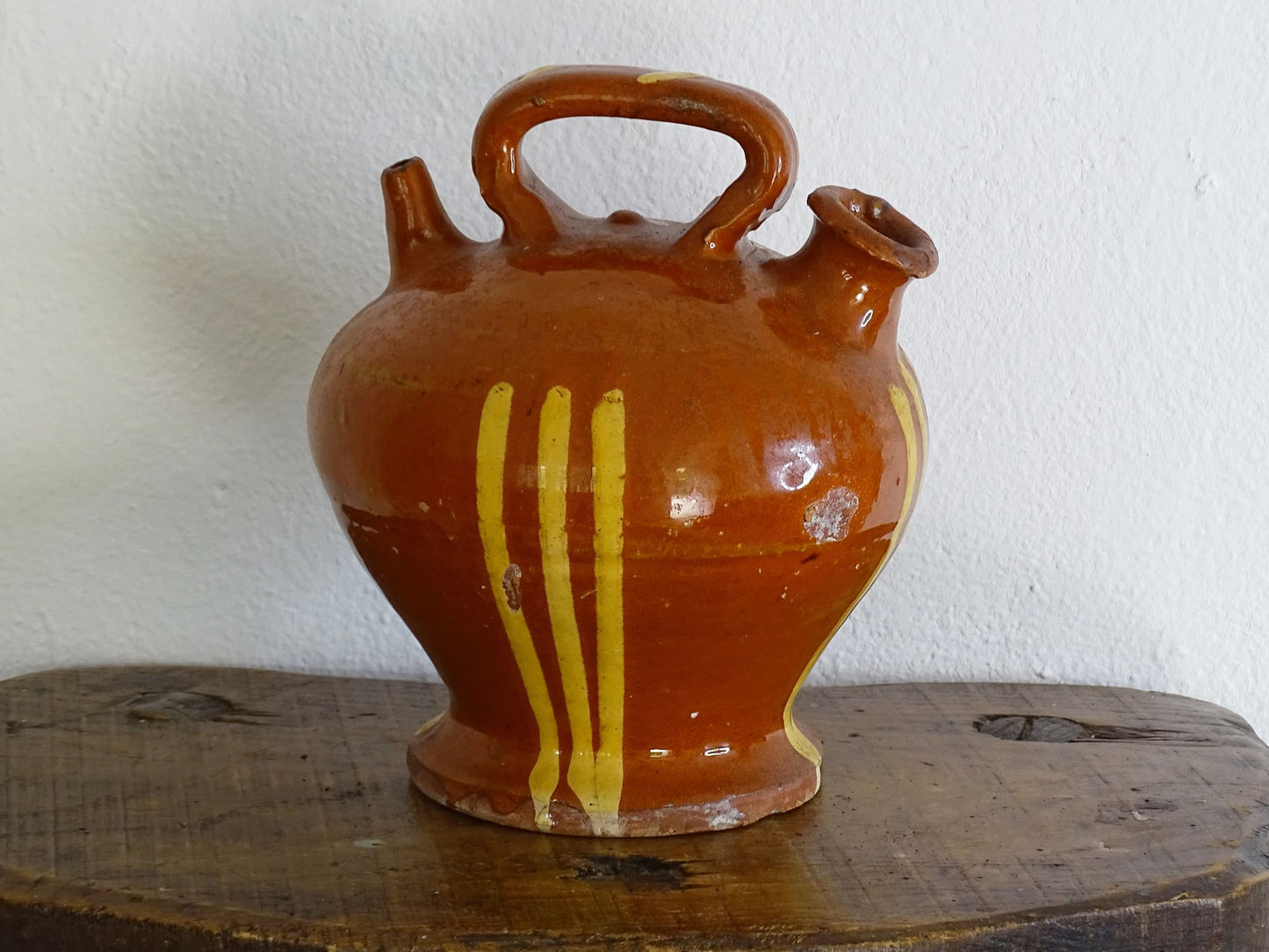 French antique pottery jug with russet glaze and yellow stripes. There is a handle to the top of this rustic terracotta earthenware pitcher and two spouts.