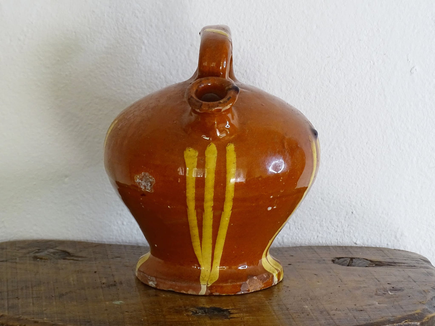 French antique pottery jug with russet glaze and yellow stripes. There is a handle to the top of this rustic terracotta earthenware pitcher and two spouts.