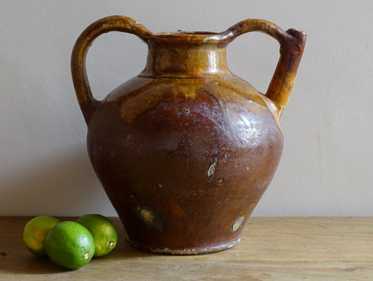 French antique pottery orjol or cruche with a golden caramel and yellow glaze. Glazed antique terracotta pitcher has two handles and a spout with a rounded body.  Earthenware pottery for an antique French farmhouse style aesthetic. 