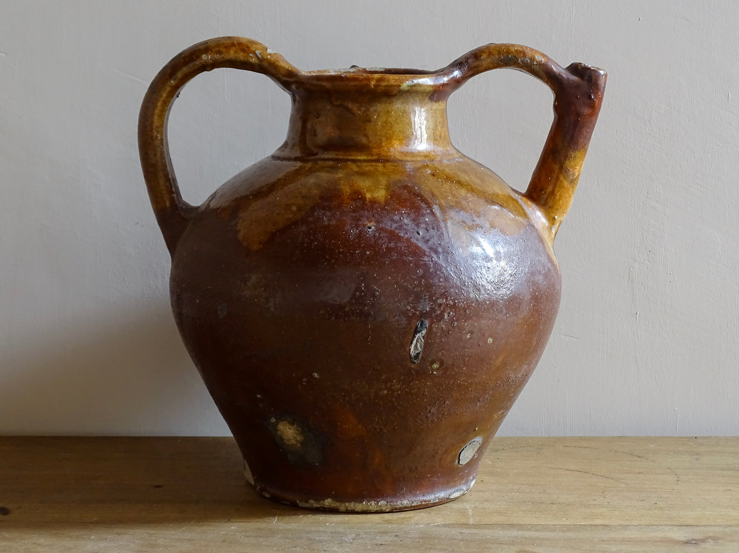 French antique pottery orjol or cruche with a golden caramel and yellow glaze. Glazed antique terracotta pitcher has two handles and a spout with a rounded body.  Earthenware pottery for an antique French farmhouse style aesthetic. 