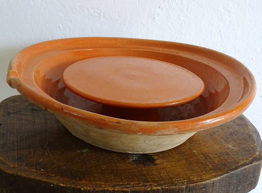 French antique pottery cheese strainer or faisseller. Shaped like a French tian bowl with a stand in the middle and a lip to the edge. Rustic French antique pottery bowl with an orange glaze. Glazed earthenware cheese drainer.