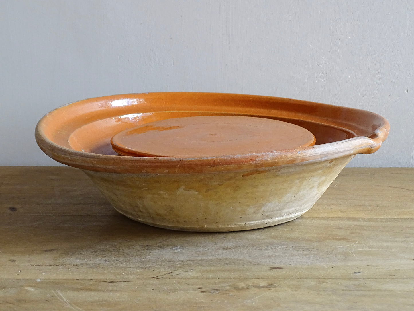 French antique pottery cheese strainer or faisseller. Shaped like a French tian bowl with a stand in the middle and a lip to the edge. Rustic French antique pottery bowl with an orange glaze. Glazed earthenware cheese drainer.