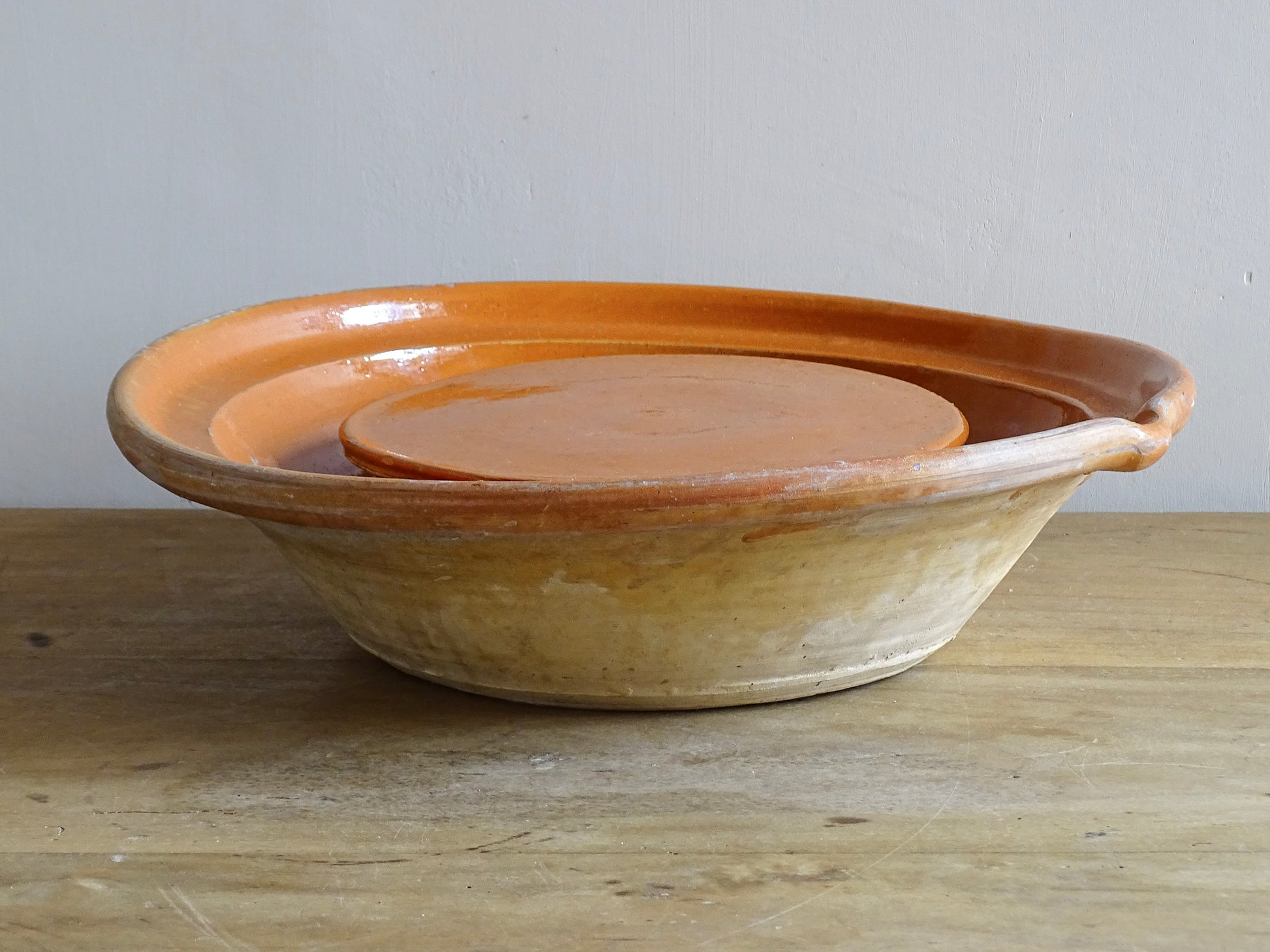 French antique pottery cheese strainer or faisseller. Shaped like a French tian bowl with a stand in the middle and a lip to the edge. Rustic French antique pottery bowl with an orange glaze. Glazed earthenware cheese drainer.