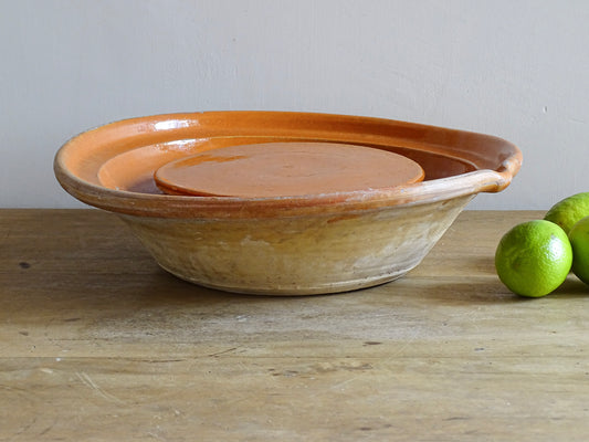 French antique pottery cheese strainer or faisseller. Shaped like a French tian bowl with a stand in the middle and a lip to the edge. Rustic French antique pottery bowl with an orange glaze. Glazed earthenware cheese drainer.