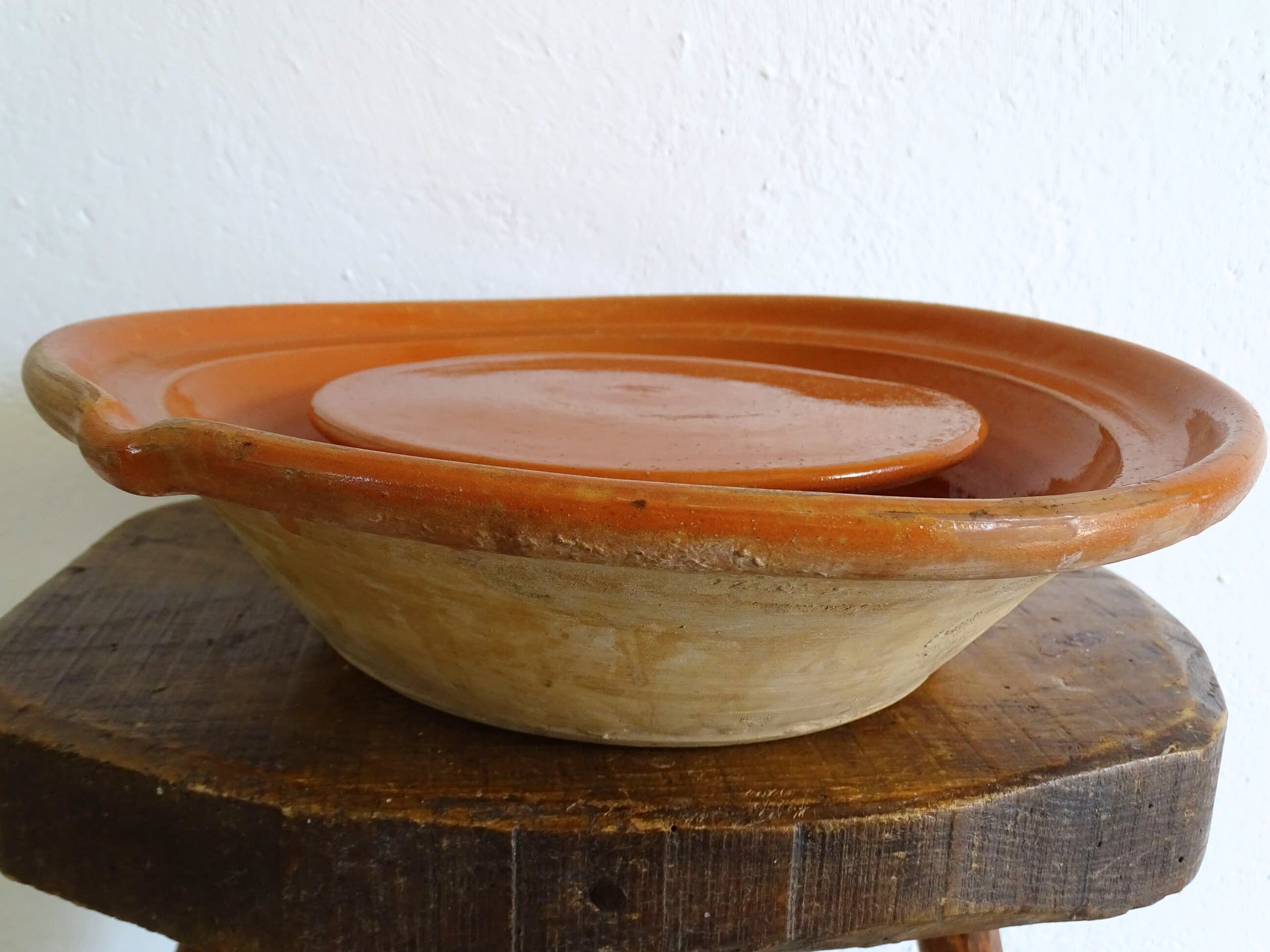 French antique pottery cheese strainer or faisseller. Shaped like a French tian bowl with a stand in the middle and a lip to the edge. Rustic French antique pottery bowl with an orange glaze. Glazed earthenware cheese drainer.