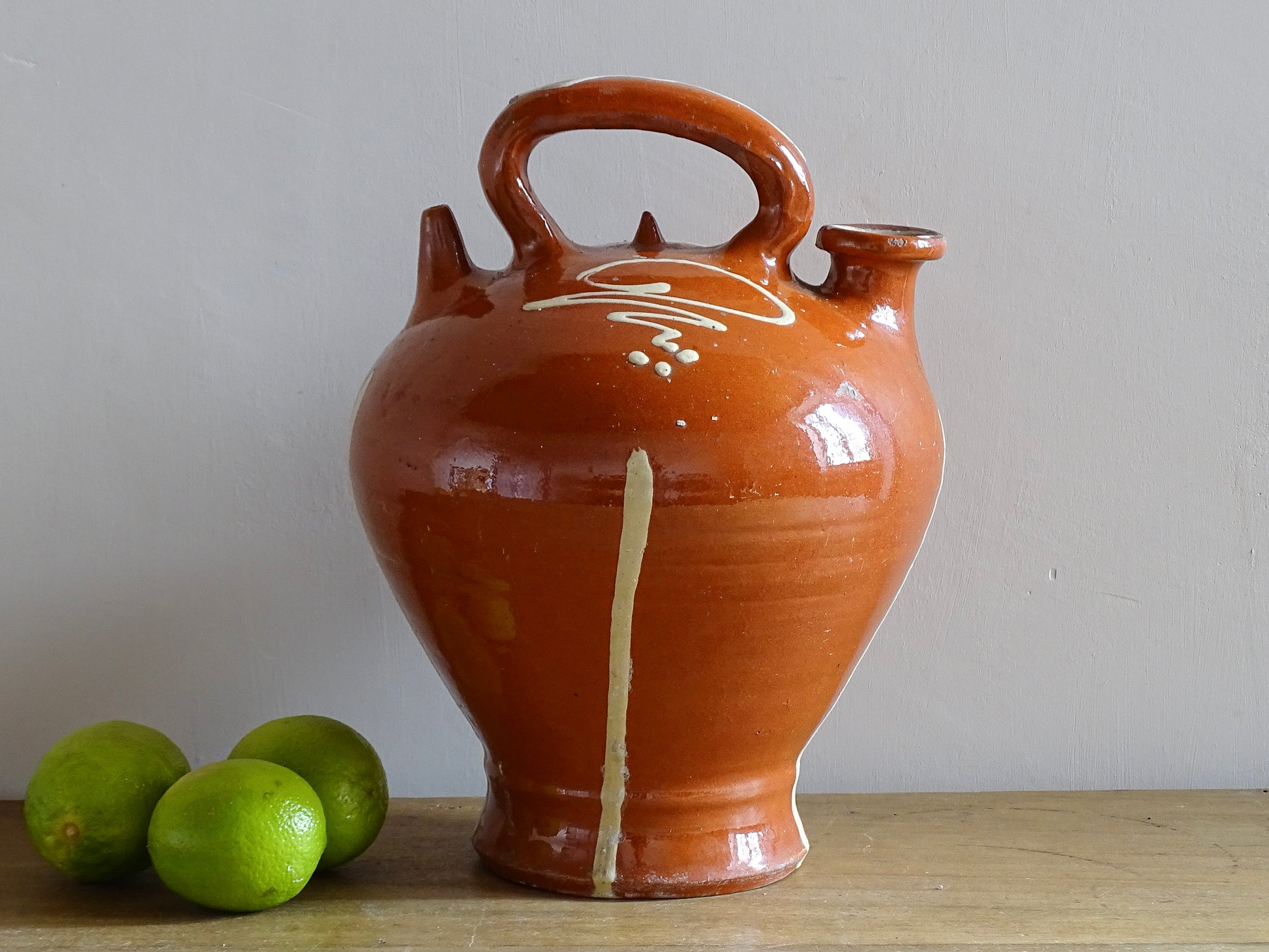 Rustic French antique pottery cruche or gargoulette with a deep red glaze and yellow stripe detailing. The body of this terracotta pitcher is a rounded shape with a handle to the top and two spouts. Glazed pottery water jug for a Provençal style farmhouse table.