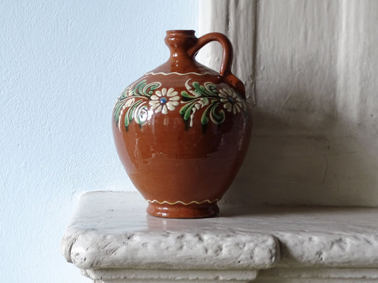 French vintage ceramic jug with an orange-red glaze and hand-painted flowers, pictured on a country house fireplace