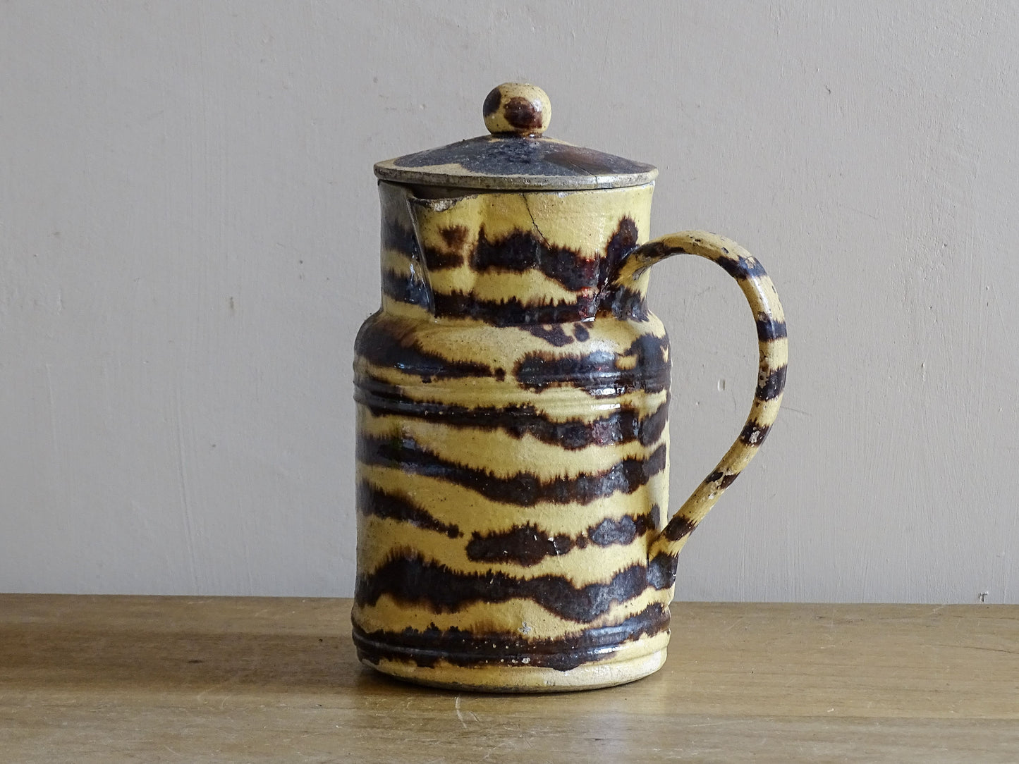 French antique ceramic jug with a lid, featuring a rustic yellow and dark brown tiger-stripe pattern.