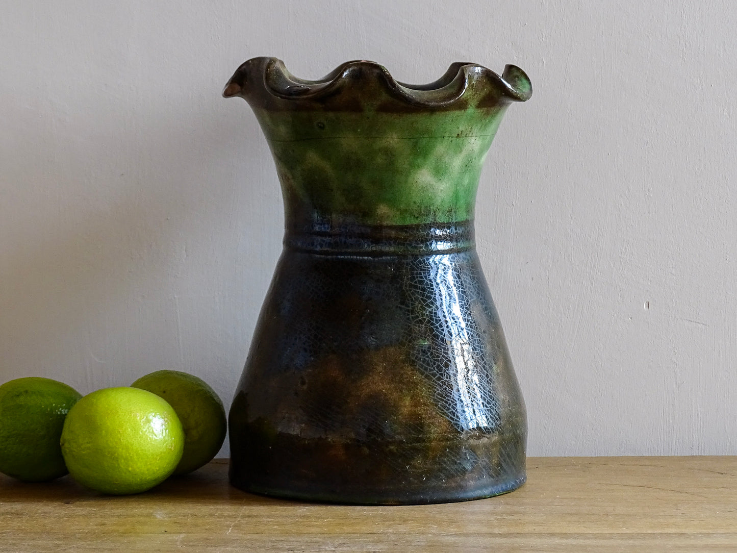 French vintage glazed terracotta vase from Castelnaudary. The ceramic vase has a textured green and brown glaze. It has a crimped rim and crackled glaze on the lower portion. Pottery vase for farmhouse decor.