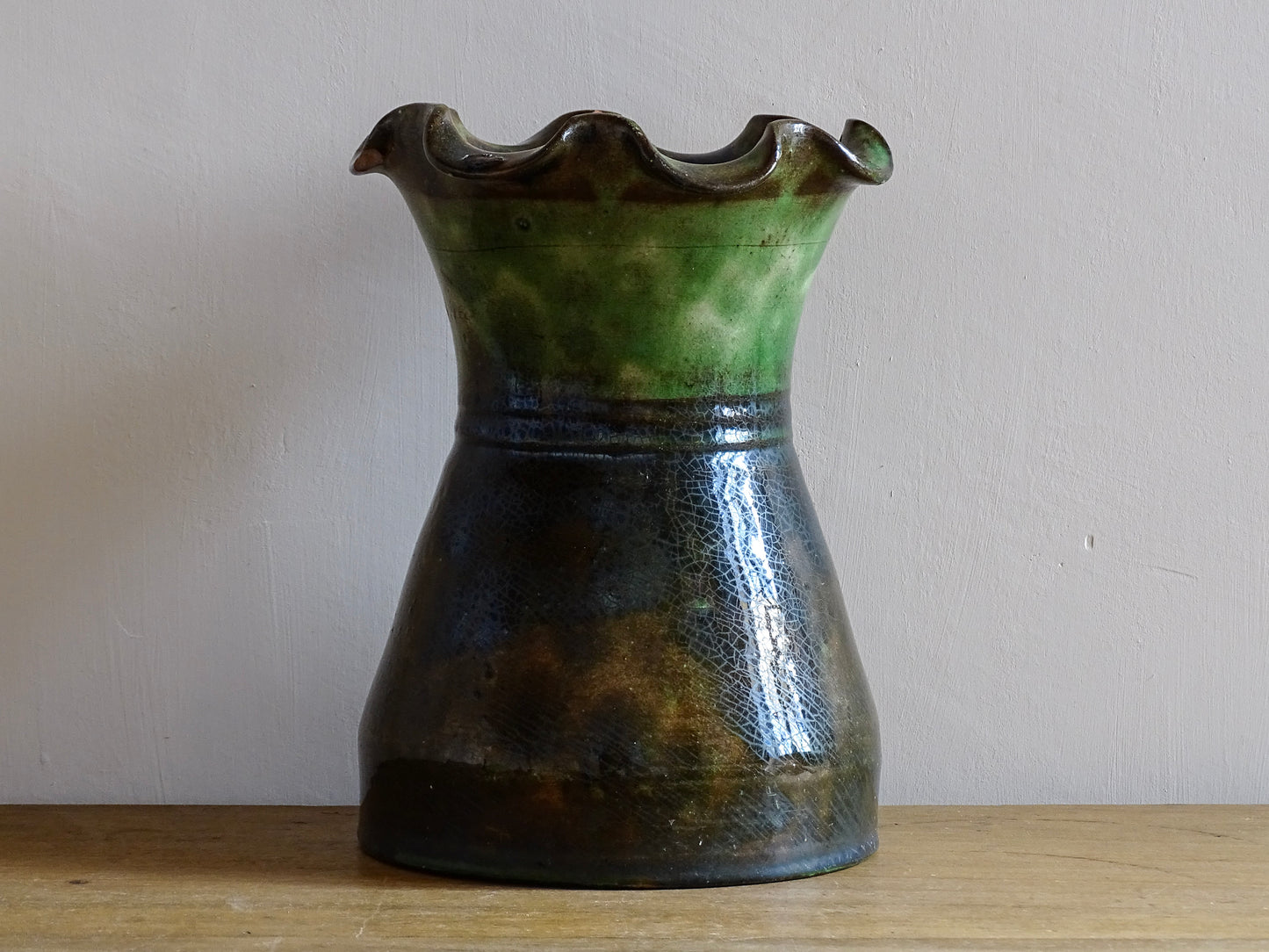 French vintage glazed terracotta vase from Castelnaudary. The ceramic vase has a textured green and brown glaze. It has a crimped rim and crackled glaze on the lower portion. Pottery vase for farmhouse decor.