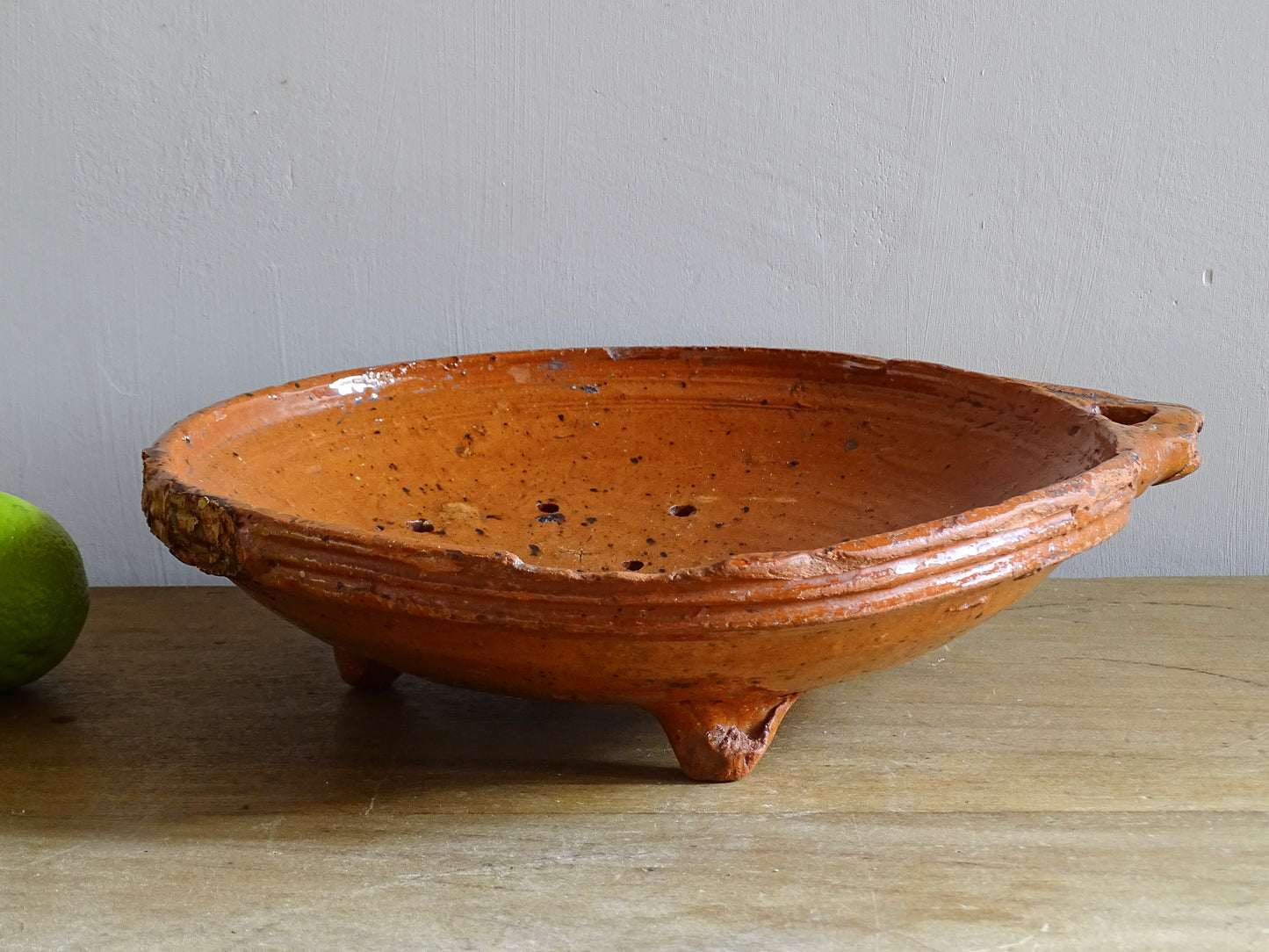 French antique terracotta sieve with orange glaze. Glazed pottery sieve on three pedestal feet. Rustic ceramic berry strainer for a farmhouse kitchen. 