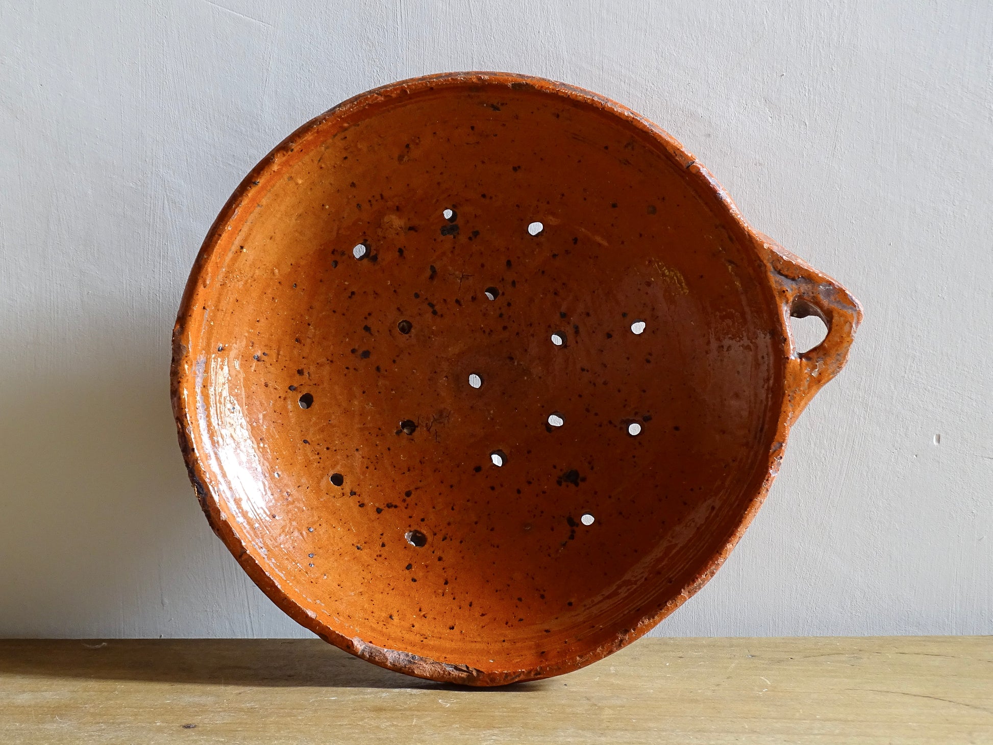 French antique terracotta sieve with orange glaze. Glazed pottery sieve on three pedestal feet. Rustic ceramic berry strainer for a farmhouse kitchen. 