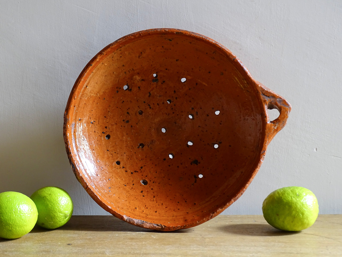 French antique terracotta sieve with orange glaze. Glazed pottery sieve on three pedestal feet. Rustic ceramic berry strainer for a farmhouse kitchen. 