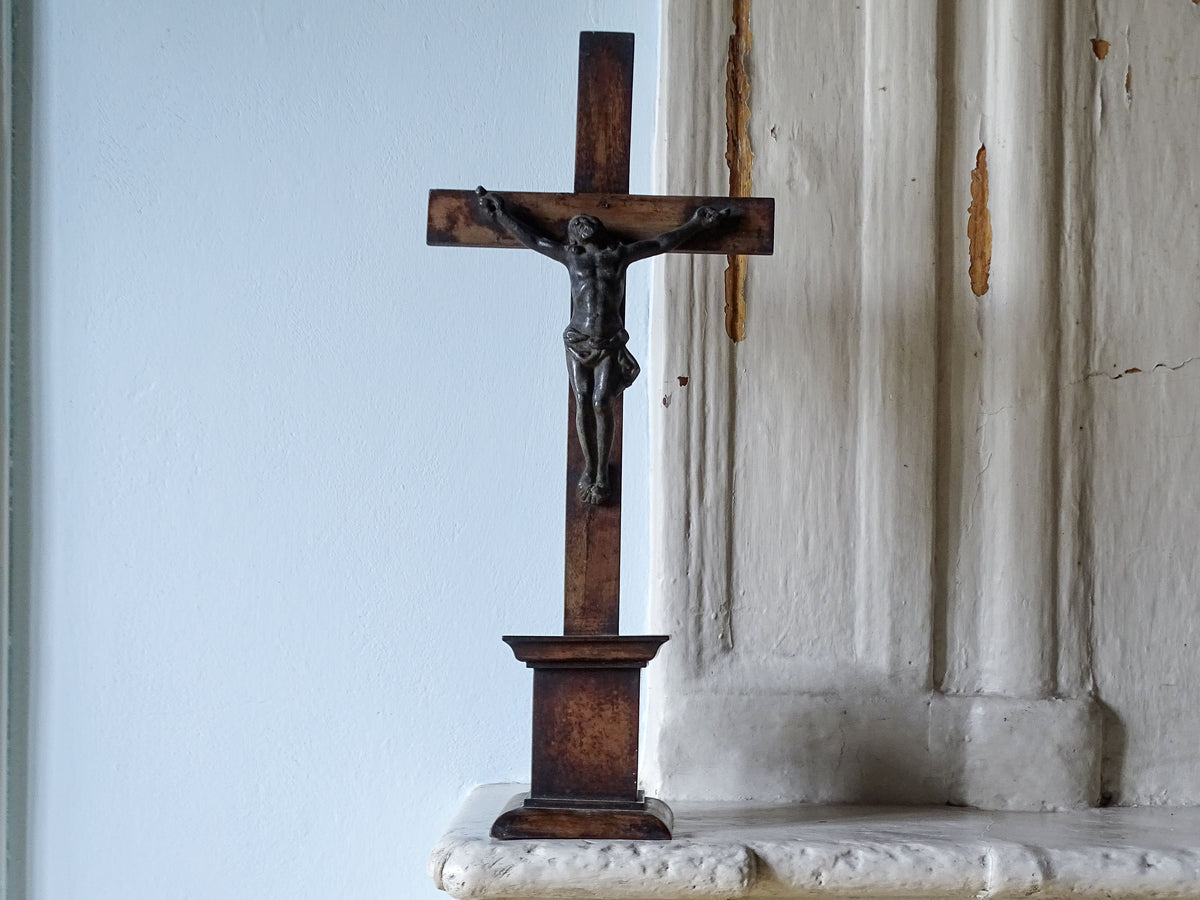 French antique wooden crucifix in dark brown with a detailed metal corpus of Jesus Christ, displayed on a country house fireplace.