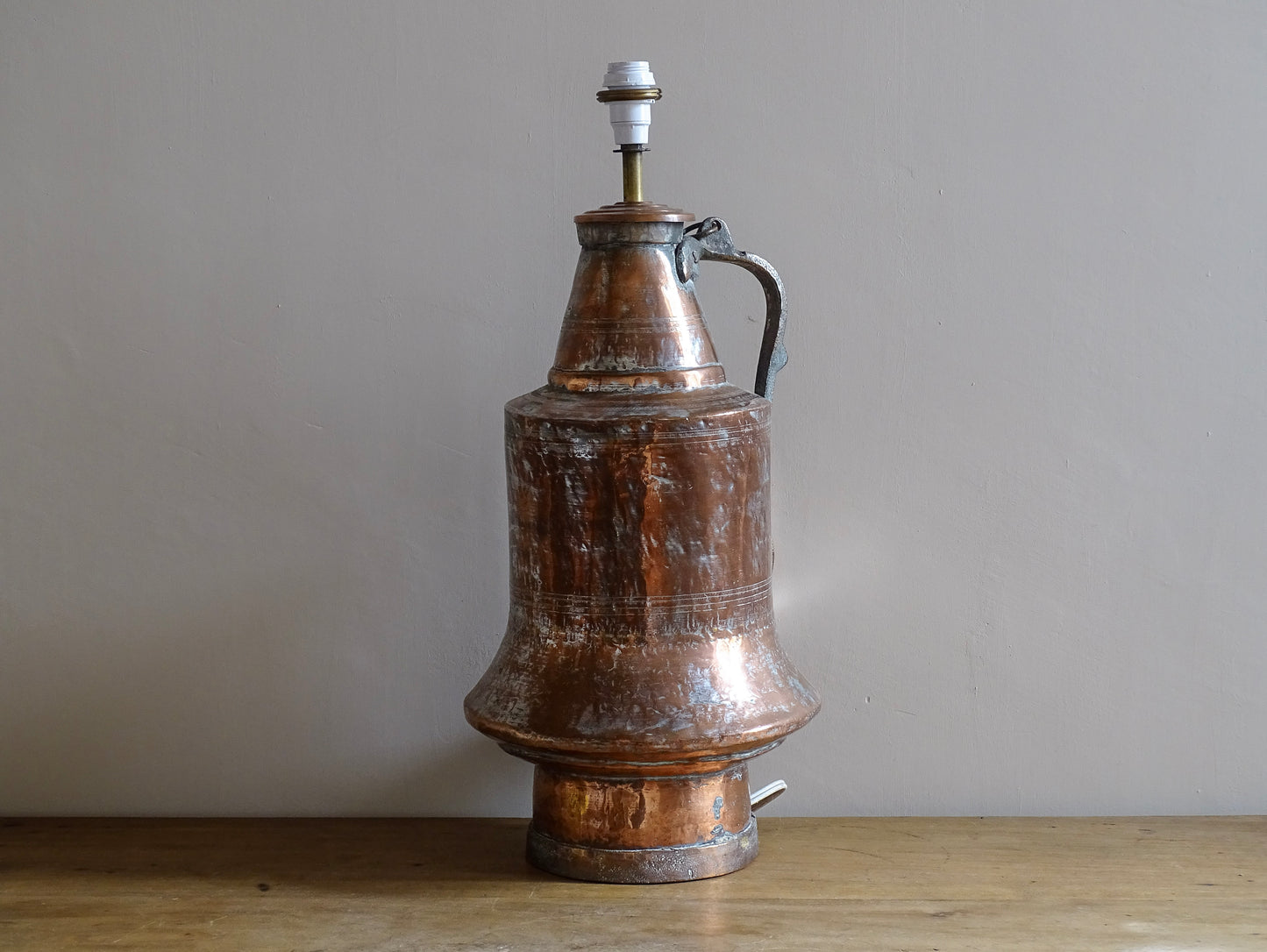 French antique copper pitcher  converted into a copper table lamp. The antique lamp has a flared base, curved handle, and surface patina.