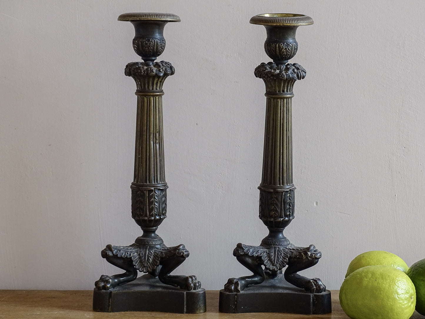 French antique bronze candle holders. French restoration period candlesticks are on a tripod base with lion paw feet and acanthus leaves. Acanthus leaves and various fruits and berries adorn the top of the reeded columns.