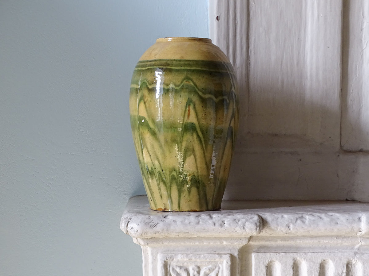 French antique earthenware vase with yellow and green glaze, displayed on a country house fireplace