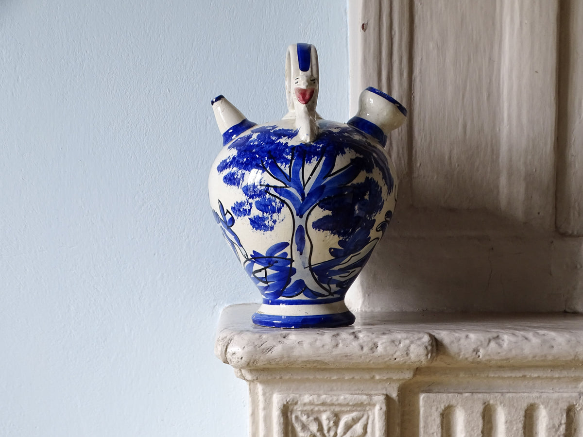Spanish vintage ceramic pitcher or gargoulette with blue and white glaze, pictured on a country house fireplace