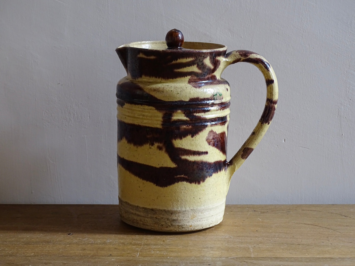 Large French antique ceramic pitcher with a lid. The glazed pottery jug has a gorgeous brown drip glaze on a yellow glazed background. 