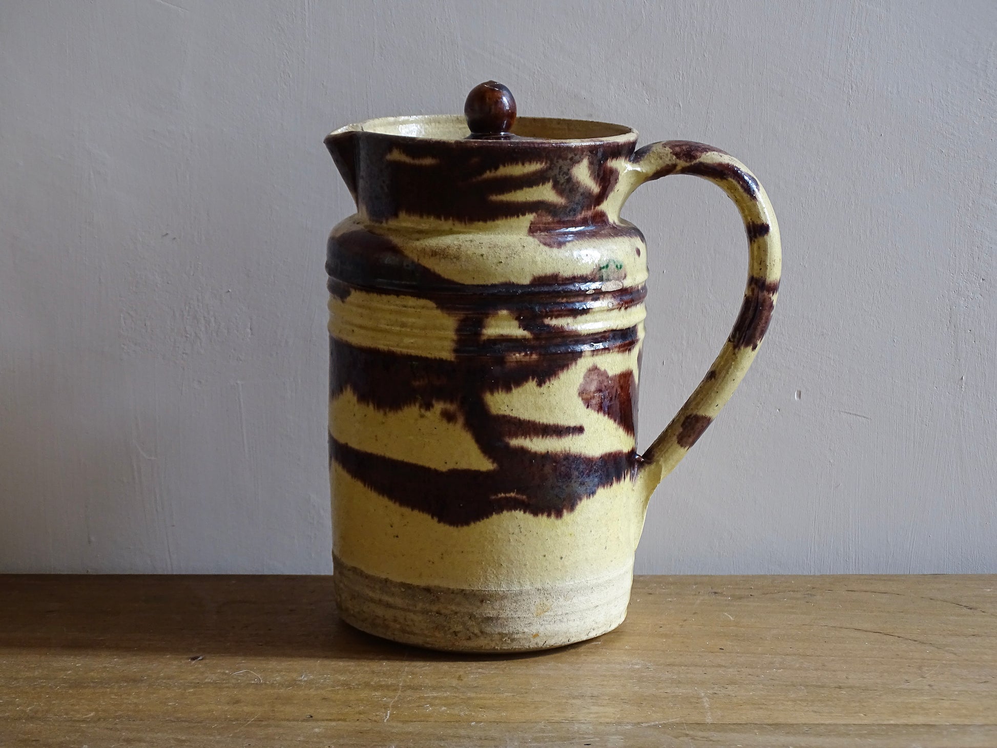 Large French antique ceramic pitcher with a lid. The glazed pottery jug has a gorgeous brown drip glaze on a yellow glazed background. 