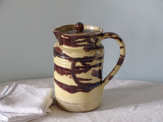 Large French antique ceramic pitcher with a lid. Glazed pottery jug with a brown drip glaze on a yellow glazed background. 