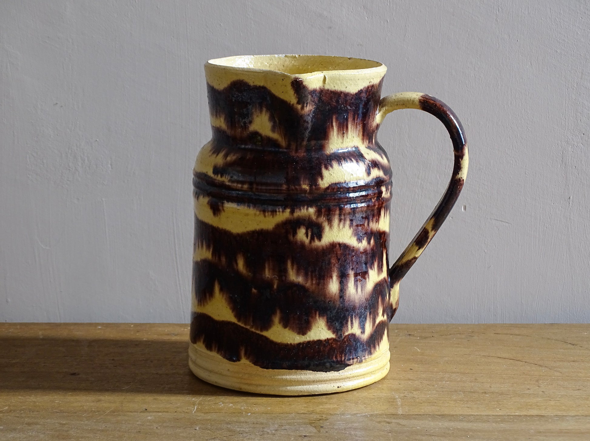Rustic French antique ceramic pitcher with yellow glaze and brown drip glaze detailing. This Dieulefit pottery jug has a handle to the side.