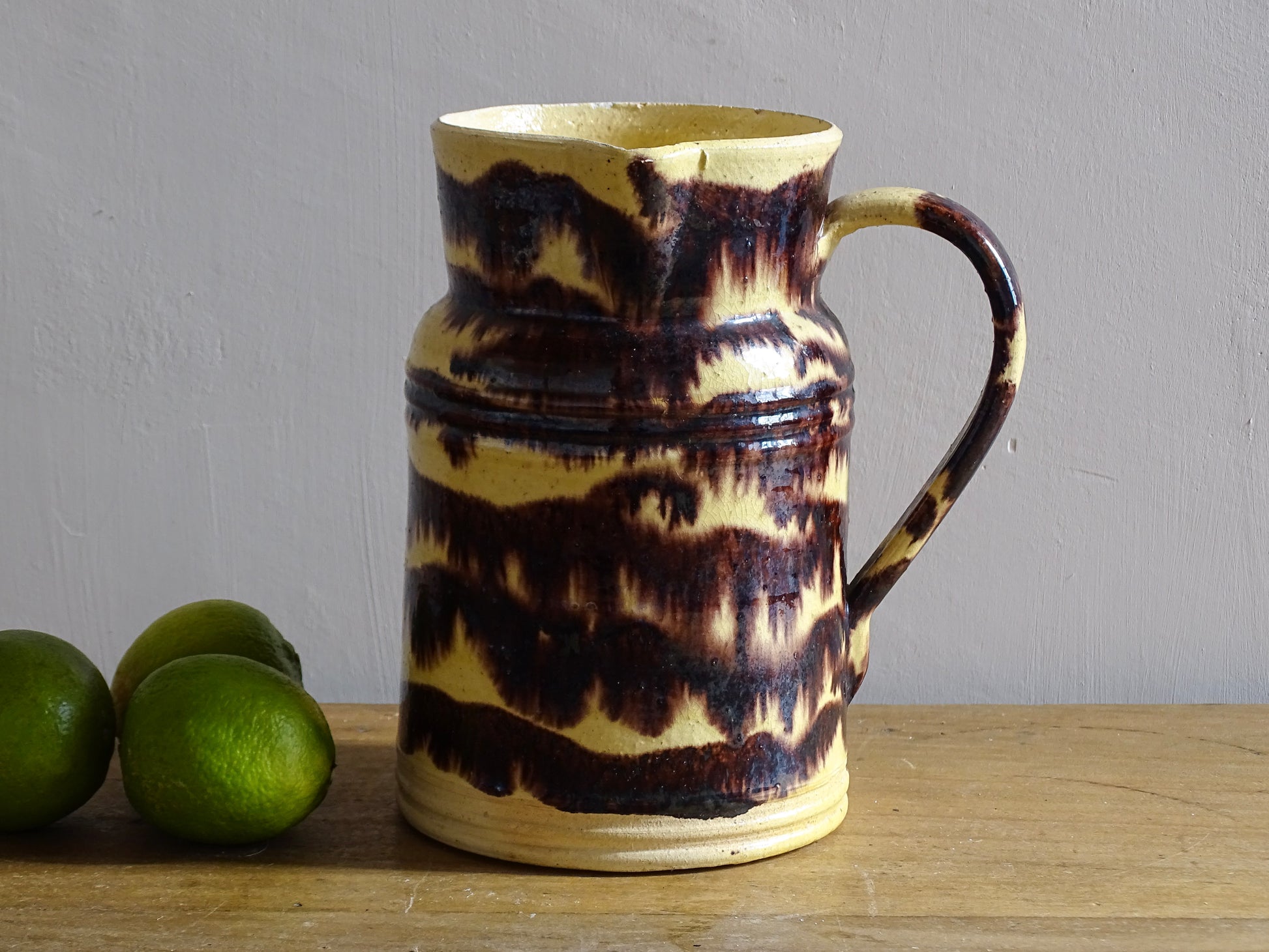 Rustic French antique ceramic pitcher with yellow glaze and brown drip glaze detailing. This Dieulefit pottery jug has a handle to the side.