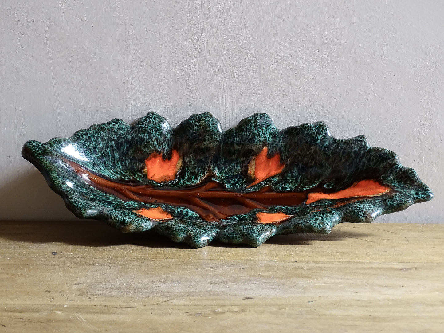 Large French vintage Vallauris ceramic bowl in the shape of a leaf. It is glazed with a dark green with details in brown and orange.